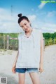 A young woman standing on a beach next to a fence.