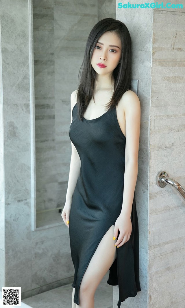A woman in a black dress leaning against a wall.