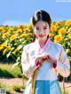A woman in a blue and white hanbok standing in front of yellow flowers.