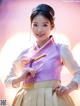 A woman in a pink and yellow hanbok poses for a picture.
