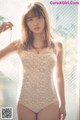 A woman in a white bodysuit posing by a window.