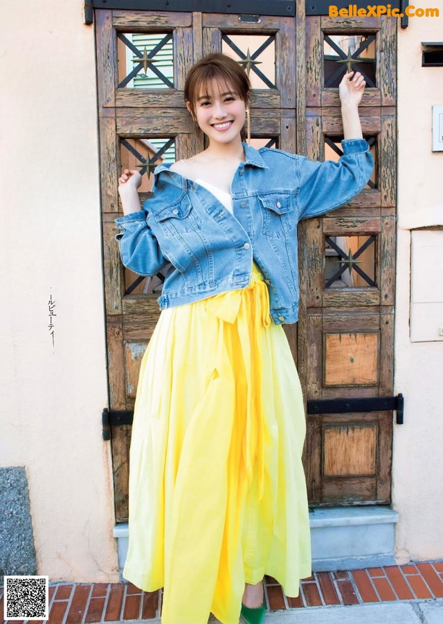 A woman standing in front of a wooden door wearing a yellow skirt.