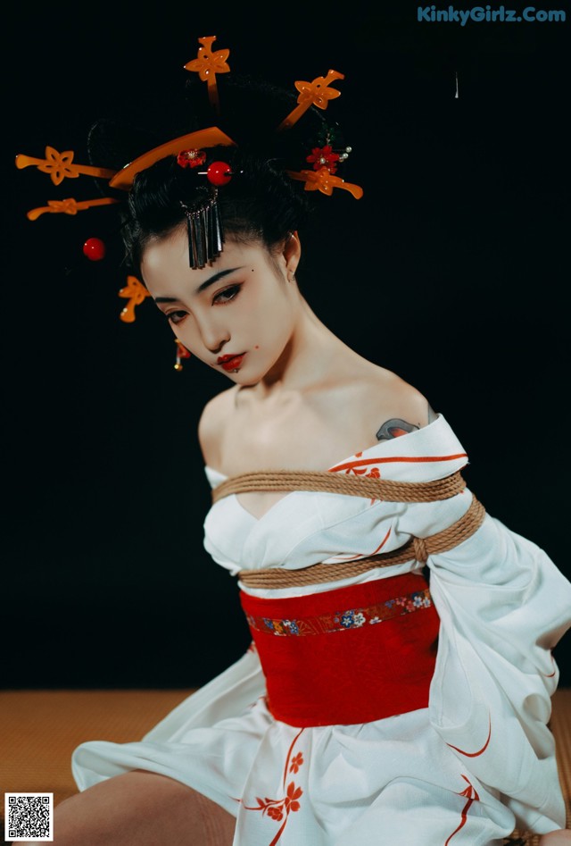 A woman in a white and red kimono sitting on a bed.